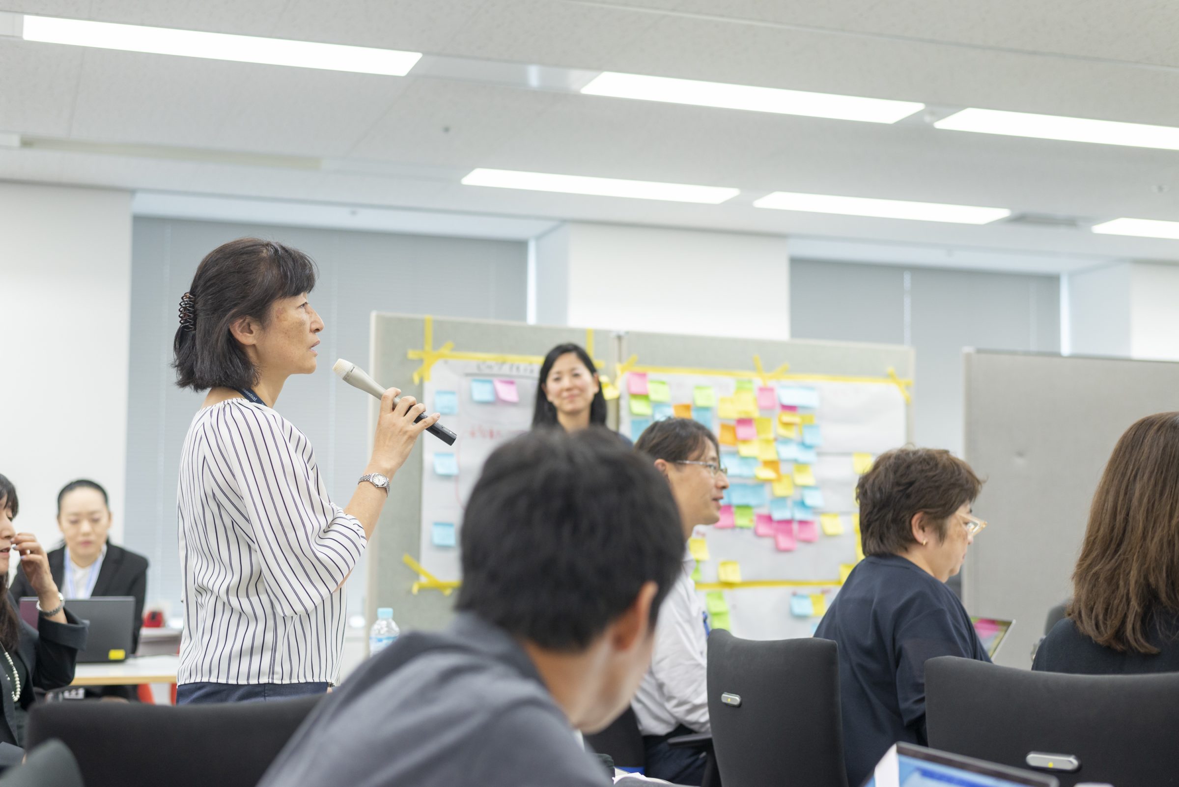 立ち上がって右手にマイクを持ち話す女性