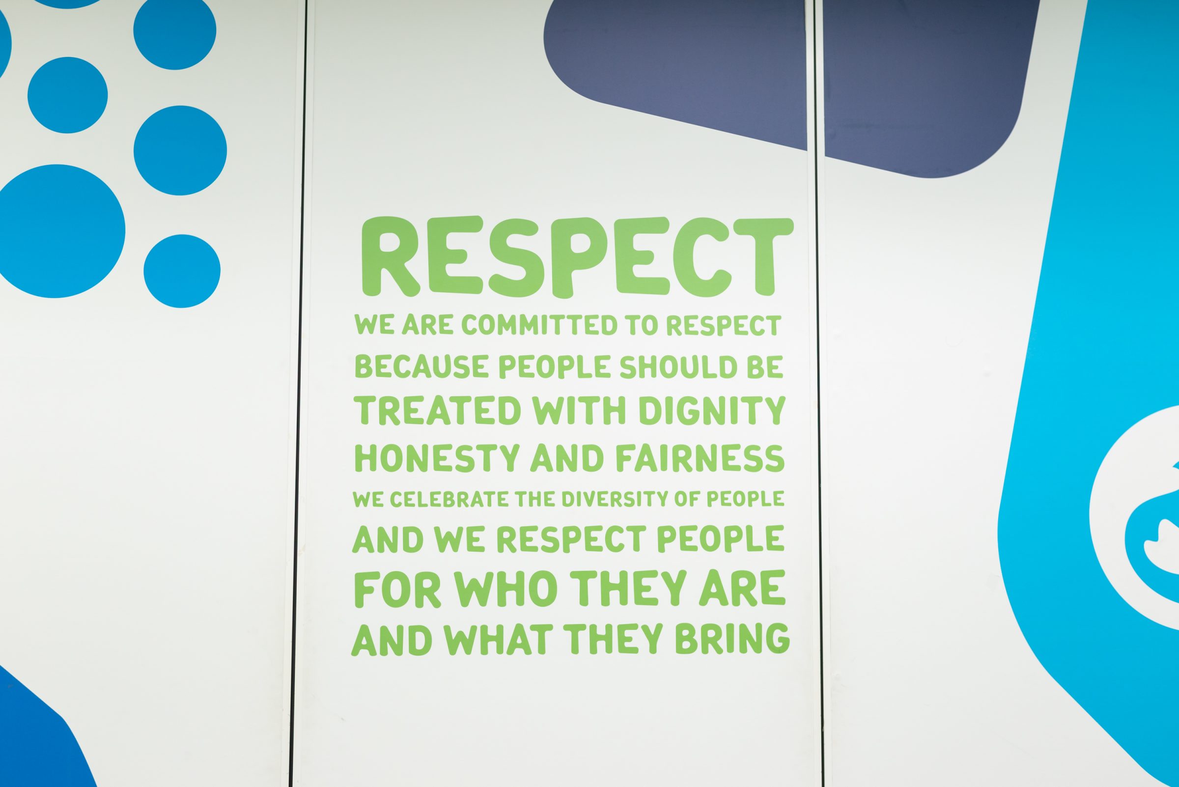 白地の壁に黄緑の文字で”RESPECT - WE ARE COMMITTED TO RESPECT BECAUSE PEOPLE SHOULD BE TREATED WITH DIGNITY HONESTY AND FAIRNESS. WE CELEBRATE THE DIVERSITY OF PEOPLE AND WE RESPECT PEOPLE FOR WHO THEY ARE AND WHAT THEY BRING”と書いてある